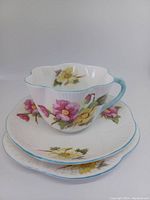The trio stacked showing the teacup on top with the saucer and dessert plate beneath, all decorated with the Begonia floral pattern and turquoise edging.