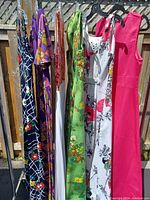 Six vintage maxi dresses hanging on a rack outside showing colors, patterns, and style details.