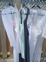 Side view of 6 lingerie pieces on hangers showing lace, sheer, satin fabrics in white, black and mint colors.