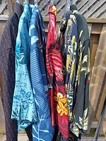 Side view of six vintage Hawaiian shirts hanging showing various colors and patterns including red, blue, black, navy and tropical prints.