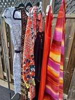Six vintage clothing items hanging on a rack outdoors, showing a variety of patterns and colors.