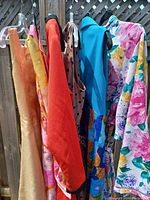 Six vintage clothing items hanging on a rack, showing various colors and fabrics including floral patterns, orange-red, beige with polka dots, and plain tan.