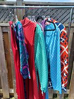 Eight vintage clothing items hanging on a rack featuring vibrant and varied colors and patterns.