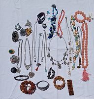 Full view of 30 assorted vintage costume jewelry pieces arranged on a white background, showing necklaces, bracelets, brooches, rings, and pins with various colors and materials.
