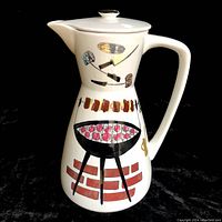 Front angled view of white ceramic coffee server with BBQ print showing a grill, meat skewer, and BBQ tools