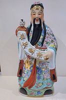 Front view of the large ceramic Chinese immortal statue showing hand-painted details, facial features, and the scroll with Chinese characters.