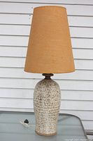 Front view of mid-century pottery lamp with tall tapered burlap shade, speckled stoneware body on gray surface.