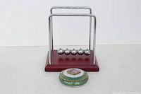 Photo showing the Limoges trinket box and the Newton's cradle desk toy side by side on a clear background.