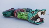 Side angle view of the serpent figurine showing open mouth with detailed teeth and tongue, painted in turquoise, red, and green with geometric designs.