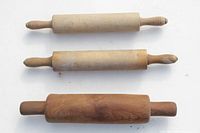 Three wooden rolling pins laid out horizontally on white surface showing their handles and barrels.