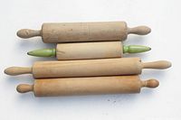 Photo showing four wooden rolling pins arranged horizontally, two with natural wood handles, two with green painted handles, displaying signs of wear and use.