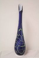 Front view of tall slender blue glass vase with green drizzle pattern