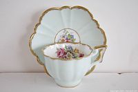 Front view of teacup showing floral interior and gold trim with matching scalloped saucer behind