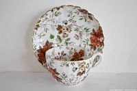 Side and front view of teacup placed inside saucer, showing floral pattern and gold trim.