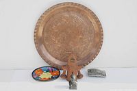 Overview of lot showing large copper plate, colorful pottery plate, wooden clackers, small figurine, and metal belt buckle.
