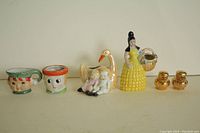 Set of five vintage ceramic holders and shakers shown together including yellow woman figurine, swan with children, gold-toned shakers, and two small face holders.