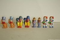 Seven vintage ceramic salt and pepper shakers arranged in a row showing all designs: orange anthropomorphic figures in top hats, colorful parrots, lavender floral tall shakers, and ceramic girls holding vegetables.