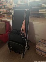 Black folding AeroPilates Pilates bench standing folded, showing the frame, cushioning, and accessories hanging on it.