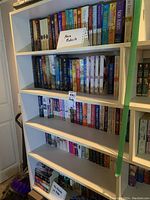 Five white shelves filled with hard and paperback books including authors Nora Roberts and J.D. Robb.