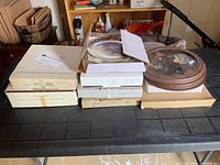 Nine collector plates in original boxes stacked on a table, showing packaging and certificates inside.