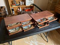 Two wood-tone storage boxes each with four shallow drawers partially open showing plates inside