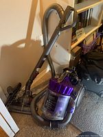 Wide view of Dyson canister vacuum with hose and power nozzle leaning against shelving unit