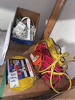 Overall lot showing extension cords bundled and one new cord in box, power bars and a white carbon monoxide detector in a box.
