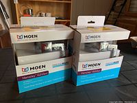 Two identical Moen Hensley towel rings in unopened retail packaging displayed on a table.