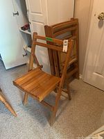 Three wooden fold-up chairs stacked against a wall, showing the overall look and size.
