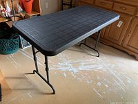 Full view of the black plastic folding table with metal legs in a room with wooden furniture and some scattered items on the floor.