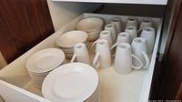White porcelain dinner plates, bread plates, salad plates and mugs, arranged in drawer.