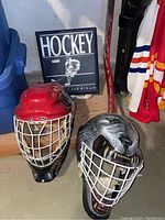 Two goalie helmets, hockey card album visible behind them, concrete floor setting.