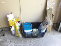 Photo showing two large yellow and white bags of Deep Frost ice salt, a blue and white plastic container, and plastic salt spreaders in a black basket on a concrete floor.