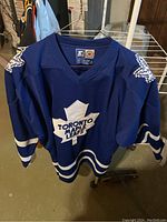 Front and shoulders of blue Toronto Maple Leafs jersey hanging, showing logos and striping