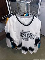 Front view of white Los Angeles Kings hockey jersey on hanger, showing team logo and visible size large.