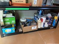 Shelf with paint cans, painting tools, and boxed light bulbs