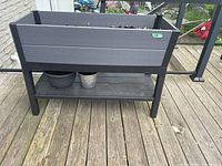 Full image of gray resin raised planter with built-in watering pipe on top and two pots on the lower shelf below it.