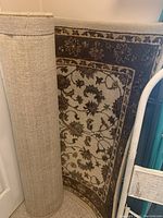Photo showing the rug rolled up next to a door with the back texture visible and the patterned side partially visible.
