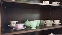 View of the variety of teacups and saucers, and pale green Depression glass butter dish and creamer set