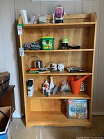 Front view of the shelving unit showing light wood finish and multiple shelves with various items on them.