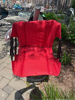 Front view of one red collapsible stadium seat placed outdoors on a paved patio with plants and garden furniture in the background.