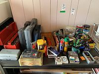Wide view of tools and containers arranged on table including toolboxes, cases, and miscellaneous small parts in plastic containers.