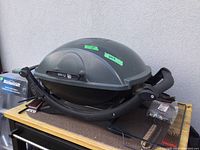 Side view of Weber Q 240 electric barbecue on wooden table with some barbecue tools around it