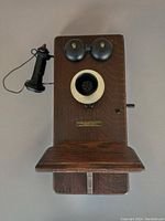 Front view of the wooden wall telephone showing twin bells, mouthpiece, earpiece, and front shelf.