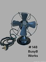 Front view of the small antique Busy B fan showing four blades, protective wire cage, base, and original braided cord with plug.