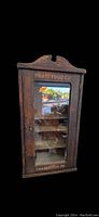 Front view of closed antique wooden cabinet with glass door showing Pratt Food Co inscription.