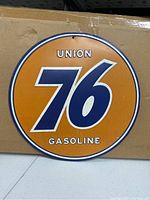Photo of a 12-inch round metal Union 76 Gasoline sign with an orange background and blue "76" logo, white text, and a small hole near the top for hanging.