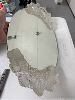 Clear overhead angled view of the oval glass vanity mirror showing the frosted glass frog feet at the top edge.