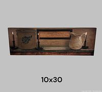 Front view of rectangular lighted canvas, 10x30 inches, showing two lit candles on either side, a decorated container, and a pitcher on a wooden shelf design.