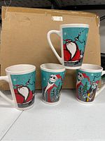 Photo showing all four ceramic Nightmare Before Christmas mugs featuring Santa Claus and Jack Skellington designs on teal backgrounds with snowflakes.